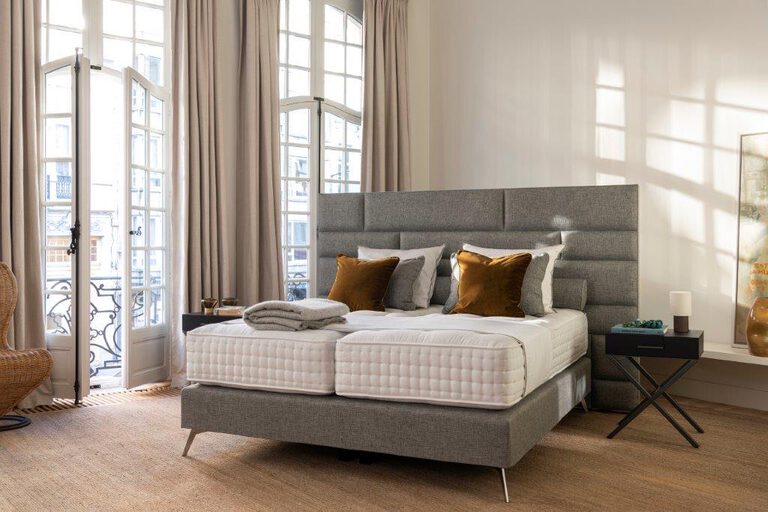 Graues Boxspringbett mit hohem, quer gestepptem Kopfteil in einem Altbauzimmer