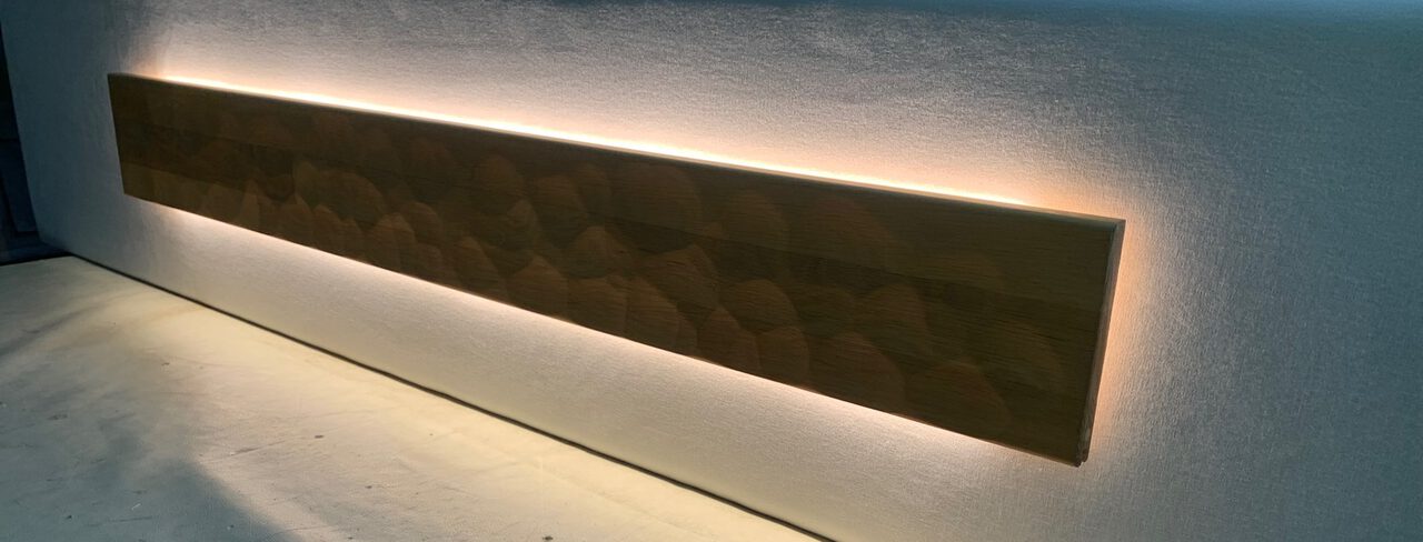 Holzblende im Kopfteil, hinter der ein warmer Lichtsaum leuchtet