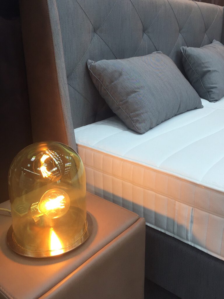 Leuchte mit Glaskuppel auf einem gepolsterten Nachttisch neben einem Bett mit gestepptem Kopfteil