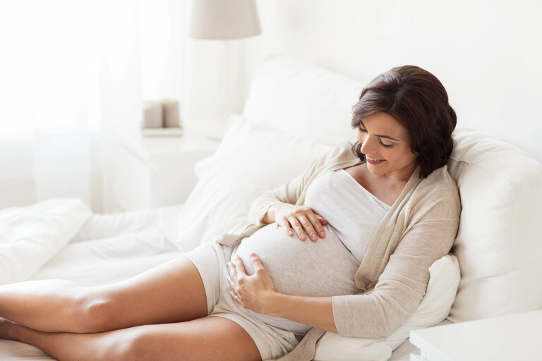 Schwangere Frau ruht sich im Bett aus und hält ihren Bauch